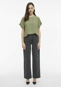 Alyvos spalvos, tekstūruotas viršus su trumpomis rankovėmis derinamas su aukštu liemeniu, plačiomis juodomis džinsomis ir juodais smailiais bateliais.