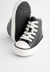 Baskets montantes noires avec embout en caoutchouc blanc et lacets, semelle en caoutchouc noire texturée avec motif étoile, accents de couture blanche.