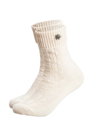 Paar cremefarbener gestrickter Knöchelsocken mit gerippten Bündchen und einem kleinen metallischen, blumenförmigen Anhänger an einem Bündchen.