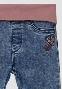 Leggings en denim avec une taille élastique rose, présentant un cœur en imprimé léopard et une broderie de cœur rouge sur la poche avant gauche.