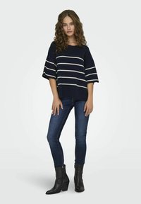 Marinrandig tröja med vida ärmar, matchad med mörkblå skinny jeans och svarta klackade ankelskor. Enkelt mönster med kontrasterande ränder.