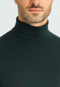Maglione a collo alto di colore verde scuro realizzato in un tessuto morbido ed elasticizzato. Presenta un collo alto e una vestibilità aderente.