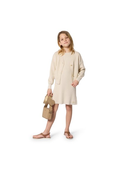 Μπεζ ριμπ φόρεμα με μακριά μανίκια και κουμπιά, σετ με αντίστοιχη ζακέτα. Αξεσουάρ περιλαμβάνουν δύο χρυσές τσάντες και σαγιονάρες.