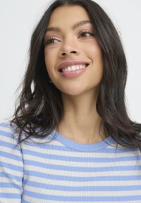 Hellblau-weiß gestreiftes, geripptes Oberteil mit Rundhalsausschnitt. Das Modell hat lange dunkle Haare und steht vor einem neutralen Hintergrund.