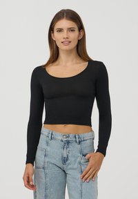 Czarny długi rękaw crop top z okrągłym dekoltem, wykonany z gładkiego materiału, połączony z jasnoniebieskimi, wysoko noszonymi, postrzępionymi dżinsami.
