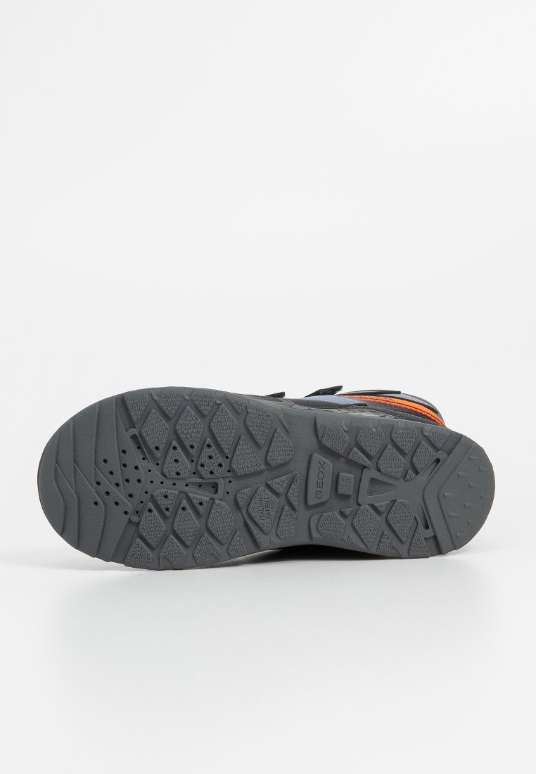 Schuhsohle aus einem dunkelgrauen Gummimaterial, ausgestattet mit einem strukturierten Profil für besseren Grip. Enthält Belüftungslöcher und ein geprägtes Logo.