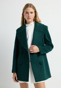 Abrigo de lana verde azulado con diseño de doble botonadura, gran cuello con muescas y botones redondos; tela texturizada y corte ajustado.
