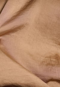 Tissu brun clair avec une texture lisse et brillante, présentant de légers plis et un léger éclat. Le matériau semble doux et fluide.