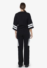 T-shirt nera oversize con strisce bianche sulle maniche, abbinata a pantaloni neri con pannelli grigi sui lati. Texture liscia.