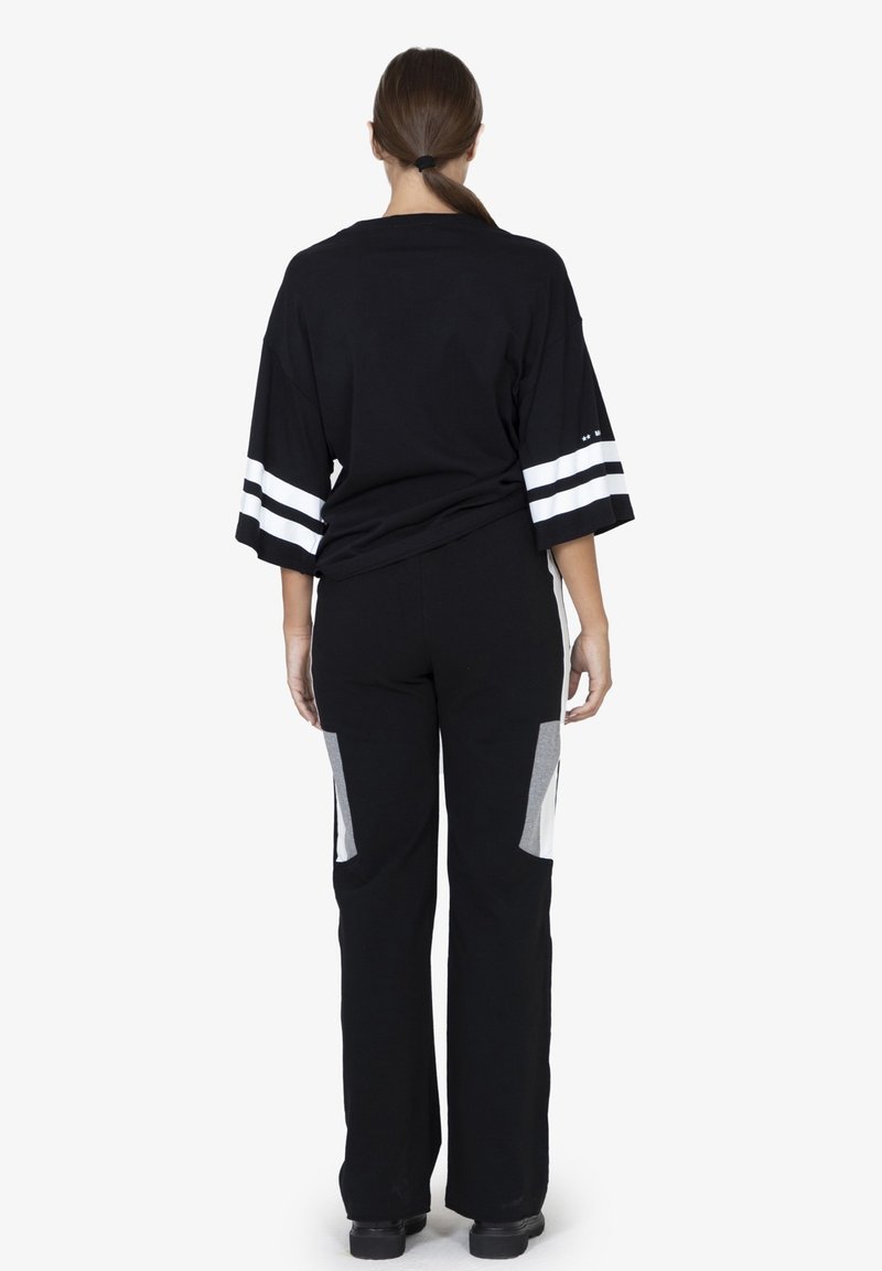 T-shirt nera oversize con strisce bianche sulle maniche, abbinata a pantaloni neri con pannelli grigi sui lati. Texture liscia.