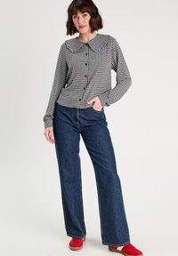 Schwarz-weißer Karo-Hemd mit langen Ärmeln und großem Kragen, Knopfleiste vorne, kombiniert mit hoch taillierten blauen Denim-Hellleg Jeans und roten Schuhen.