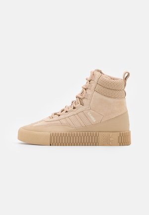 Baskets montantes beiges Adidas Samba avec semelle texturée, doublure en mesh au niveau de la cheville, lacets et languette au talon.