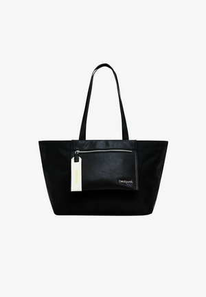 Zwarte tote bag met lange handvatten, voorzien van een voorste ritsvak en een wit label, gemaakt van een glad, mat materiaal. Minimalistisch ontwerp.