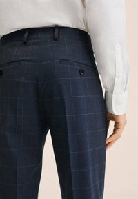 Tmavě modré kostkované kalhoty z texturované látky, s dvěma zadními kapsami na knoflíky a zúženým střihem.