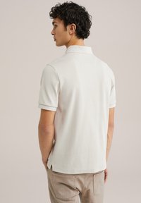 Balta ribota īsās piedurknes polo krekls ar apkakli, ar sānu slitiem un teksturētu virsmu, saskaņots ar gaiši bežām biksēm.