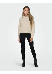 Pull crème avec un col zippé à mi-hauteur, texture côtelée et ourlet. Associé à un pantalon noir ajusté et des bottes noires brillantes.