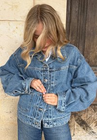 Denim jas met een ontspannen pasvorm, knoopsluiting aan de voorkant en grote zakken. Lichtblauwe kleur met subtiele vervaging en zichtbare stikseldetails.