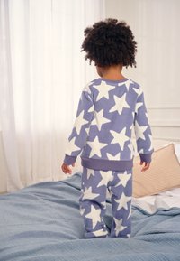 Lilla fleecetøjsæt med store hvide stjernemønstre. Overdelen har ribbet kant ved ærmerne, og bukserne har elastisk linning.