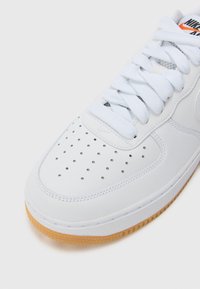 Valkoiset nahkakengät, joissa on reikäpohja, teksturoitu valkoinen nauhoitus ja kumipohja. Nike Air -brändäys näkyy kielellä.