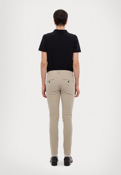 Pantaloni beige dalla vestibilità slim, realizzati in tessuto misto cotone, dotati di due tasche posteriori e un dettaglio con zip, abbinati a una polo nera.