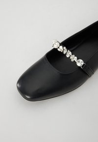 Ballerina in pelle nera con punta quadrata e una fascia decorativa con strass trasparenti che attraversa la parte anteriore.