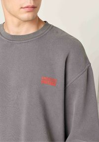 Halli puuvillane sulejope, millel on madalad õlad, ümmargune kaelus ja punane "AMERICAN VINTAGE" logo vasakul rinnal. Pehme tekstuur.