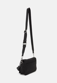 Czarna torba na ramię w kształcie prostokąta, z materiału tekstylnego, z regulowanym paskiem, srebrnymi akcesoriami i zapięciem na klapkę.