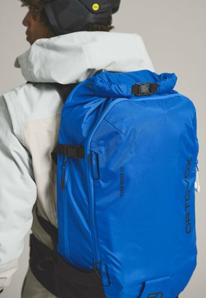 Blue backpack with a textured finish, featuring multiple zip pockets and adjustable straps. Marked with "ORTOVOX FREE RIDER 28."