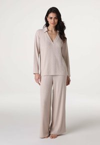 Set di abbigliamento da loungewear in maglia color beige chiaro, con maniche lunghe, colletto a V e motivo a cavo testurizzato; pantaloni a gamba larga che scivolano fino ai piedi nudi.