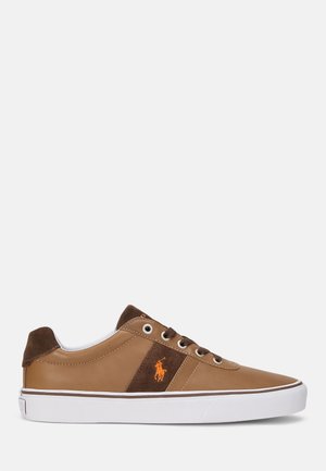 Zapatilla baja de cuero marrón con detalles en ante marrón oscuro, logo de jugador de polo naranja y suela de goma blanca con raya marrón.