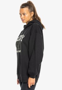 Übergroßer schwarzer Hoodie aus Baumwolle. Ausgestattet mit einem Frontdruck in Weiß und Hellgrün. Mit einer Kapuze mit Kordelzug und gerippten Bündchen.