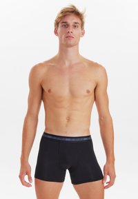 Schwarze Boxershorts aus Baumwolle, mit einem grauen elastischen Bund, auf dem der Text "JBS UNDERWEAR" steht. Enganliegendes Design mit einer glatten Textur.