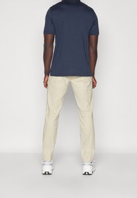 Mörkblå kortärmad t-shirt, tillsammans med krämfärgade byxor, sedd bakifrån. Outfitten fulländas med vita sneakers.