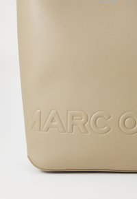 Borsa tote in pelle beige con logo "MARC O" in rilievo, texture liscia, forma strutturata e angoli arrotondati. Design semplice e moderno.