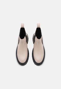 Botas de tobillo de cuero en beige claro con paneles elásticos negros a los lados y suelas de goma negra gruesas; cuenta con una pestaña en la parte trasera.