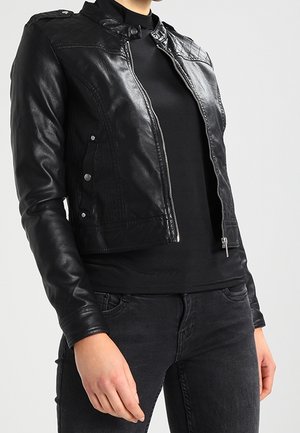 Veste en cuir noir au design court, avec des accents aux épaules, une fermeture éclair à l'avant et une texture lisse. Portée sur un haut noir.