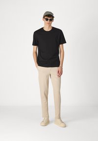 Sort bomulds T-shirt, lys beige strækbukser og cremefarvede sneakers. Accessories inkluderer en grå kasket og sorte solbriller. Minimalistisk design.