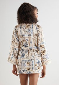 Cremefarbener Satin-Roben mit floralem Muster, das blaue und braune Akzente aufweist. Sie hat lange Ärmel, einen Taillengürtel und einen knielangen Schnitt.