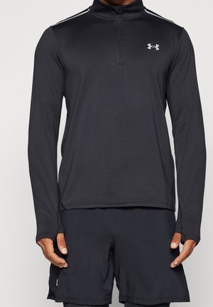 Hombre vistiendo un pulóver negro de manga larga de Under Armour con cremallera y pantalones cortos deportivos negros contra un fondo liso.