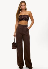 Pantalon ample marron associé à un haut bandeau à sequins foncés ; comprend un sac à main texturé et des talons aiguilles ornés de nœuds.