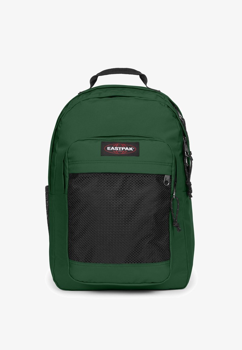 Zielony plecak wykonany z trwałego materiału, z czarną siatkową kieszenią z przodu, wyposażony w uchwyt u góry oraz regulowane, wyściełane ramiączka.