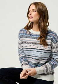 Sweter robiony na drutach z różnorodnymi wzorami w jasnym niebieskim, różowym, czarnym i białym kolorze. Posiada prążkowany biały dół i mankiety oraz okrągły dekolt.