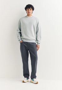 Jasnoszara bluza z prążkowanymi mankietami, zestawiona z ciemnoszarymi spodniami i białymi trampkami z zielonymi akcentami. Prosty, luźny fason.