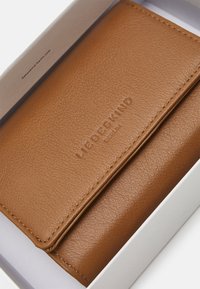 Portefeuille en cuir marron avec une finition texturée, arborant un nom de marque en relief. Présenté dans une boîte blanche.
