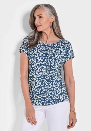 Marineblaues Oberteil mit einem weißen abstrakten Blättermuster, Rundhals, kurzen Ärmeln, aus weichem Stoff, kombiniert mit weißen Hosen.