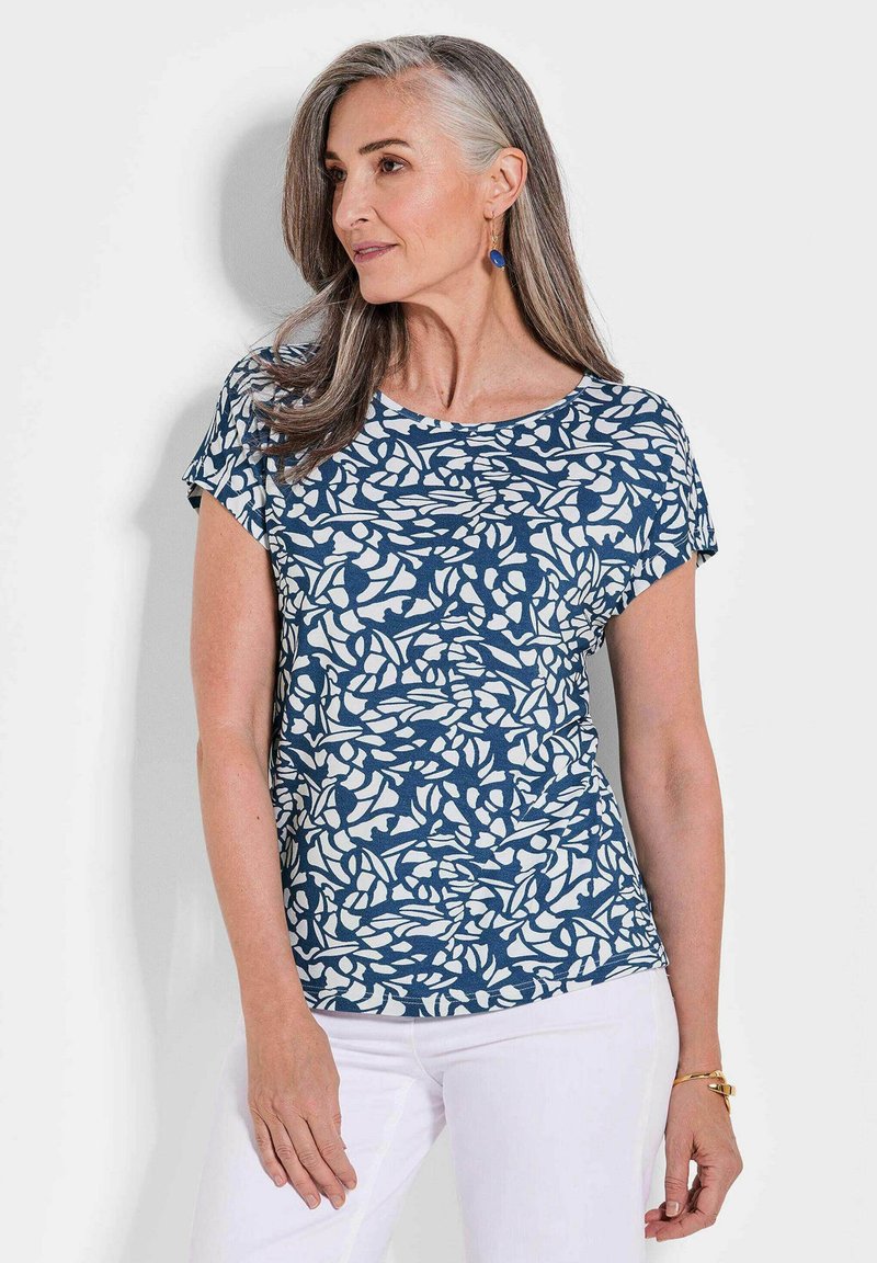 Marineblaues Oberteil mit einem weißen abstrakten Blättermuster, Rundhals, kurzen Ärmeln, aus weichem Stoff, kombiniert mit weißen Hosen.