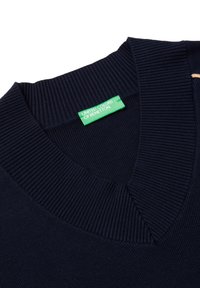 Suéter azul marino con cuello en V y textura acanalada. Etiqueta verde "United Colors of Benetton" en el cuello. Diseño simple y clásico.