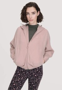 Felpa fucsia chiaro con zip intera, cappuccio con coulisse e due grandi tasche frontali. Abbinata a leggings neri con motivo a leopardo rosa.