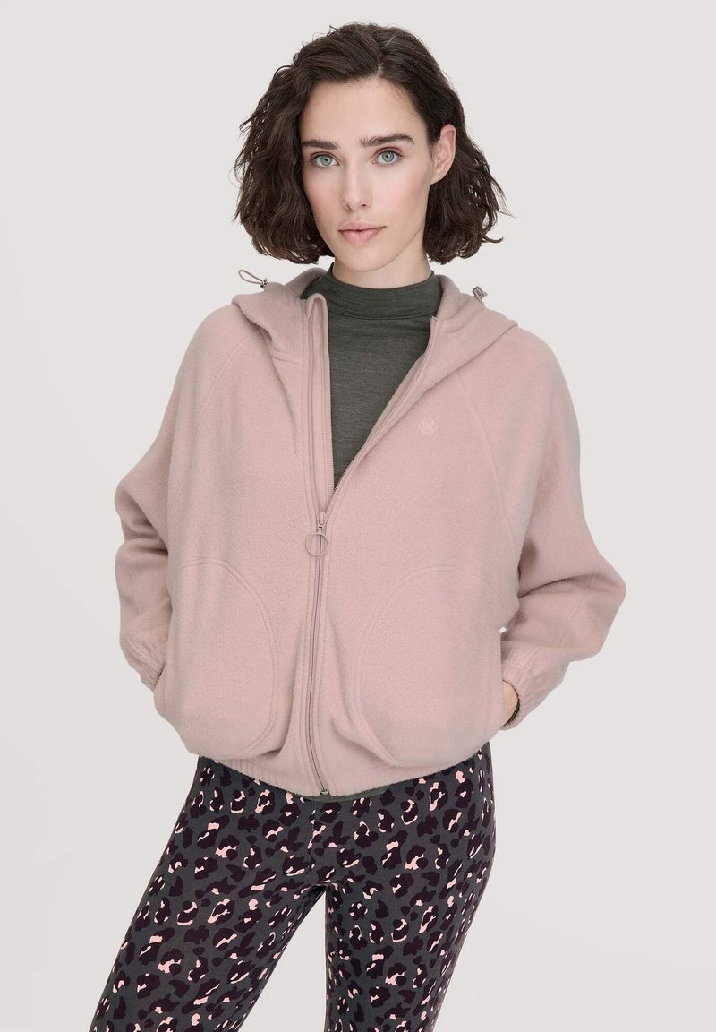 Felpa fucsia chiaro con zip intera, cappuccio con coulisse e due grandi tasche frontali. Abbinata a leggings neri con motivo a leopardo rosa.