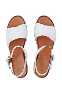 Witte leren sandalen met gekruiste banden, verstelbare enkelband en een bruine zool. Beschikt over een gladde textuur en een eenvoudig ontwerp.
